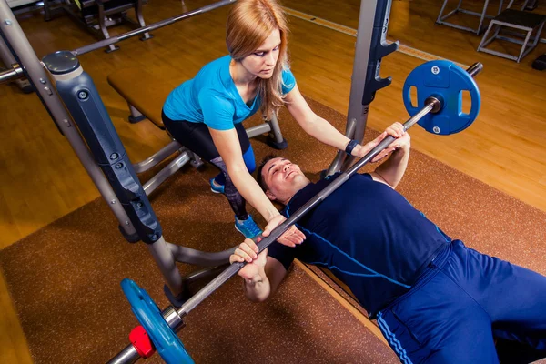 Personal Trainer hilft Männern beim Heben einer Langhantel beim Training im Fitnessstudio — Stockfoto