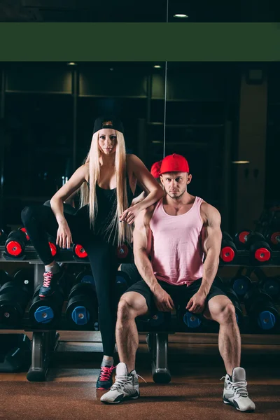 sport, bodybuilding, weightlifting, lifestyle and people concept - Young beautiful couple in stylish clothes sitting a gym near the dumbbells