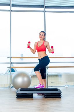 Kız adım kardiyo dumbbells ile bir spor salonunda gerçekleştirir.