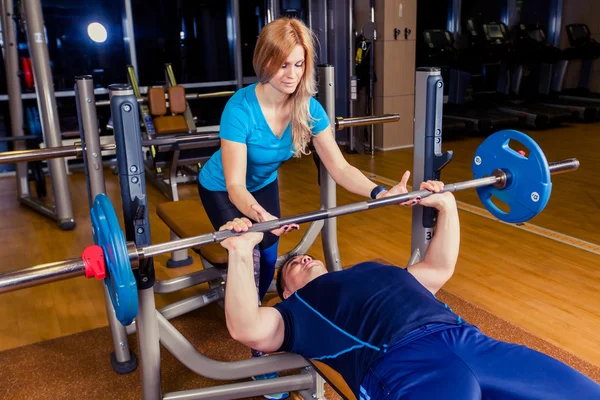 Entrenador personal que ayuda a los hombres a levantar una barra mientras hacen ejercicio en el gimnasio — Foto de Stock