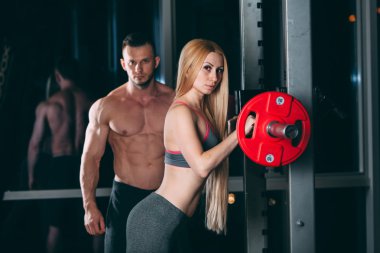 Spor salonunda ağırlık adamla egzersiz genç çift kişisel antrenör gibi görünüyor