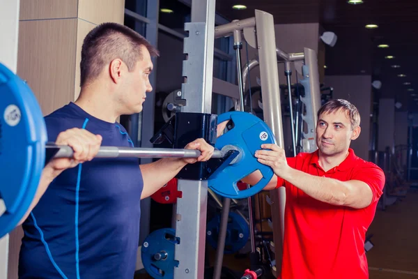 Sport, fitness, pracy zespołowej, koncepcja ludzie Kulturystyka - człowiek i osobisty trener z brzana wyginanie mięśni w siłowni — Zdjęcie stockowe