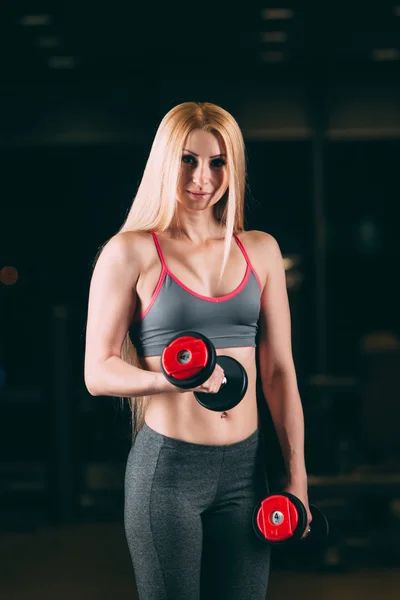 Жестокая атлетичная женщина накачивает мышцы гантелями в спортзале — стоковое фото