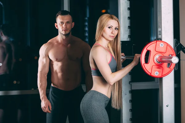 Młoda para ćwiczenia w siłowni z wagi człowieka wydaje się być osobisty trener — Zdjęcie stockowe