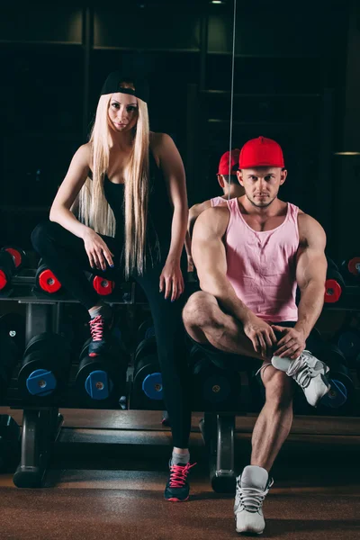 Esporte, musculação, levantamento de peso, estilo de vida e conceito de pessoas - Jovem casal bonito em roupas elegantes sentado um ginásio perto dos halteres — Fotografia de Stock