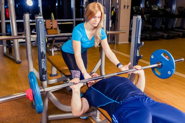 Entrenador personal que ayuda a los hombres a levantar una barra mientras hacen ejercicio en el gimnasio — Foto de Stock