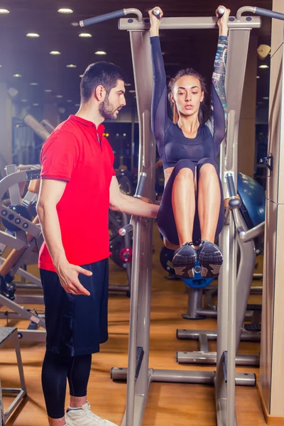 Fitness, deporte, entrenamiento y concepto de personas - Entrenador personal que ayuda a las mujeres que trabajan con músculos abdominales a presionar la barra horizontal . —  Fotos de Stock
