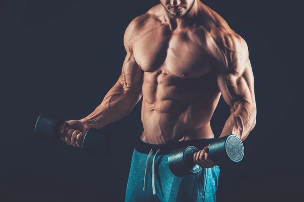 Closeup of a muscular young man lifting dumbbells weights on dar — Stock Photo, Image