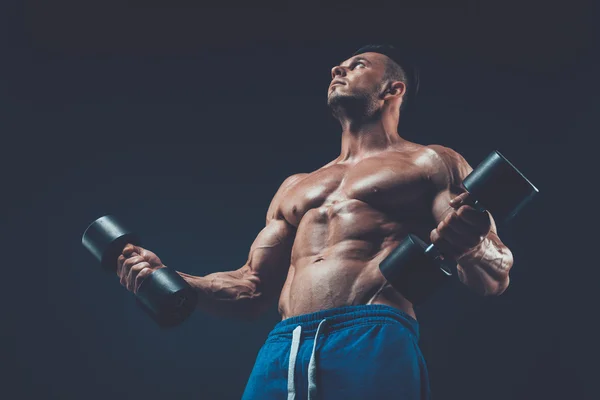 Closeup of a muscular young man lifting dumbbells weights on dar — Stock Photo, Image