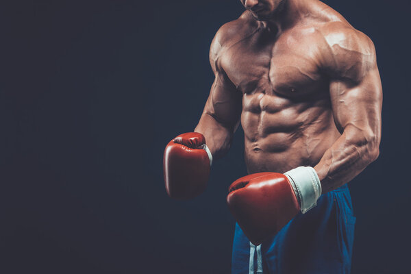 Muscular boxer in studio shooting, on black background.