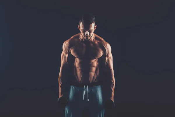 Closeup of a muscular young man lifting dumbbells weights on dar — Stock Photo, Image