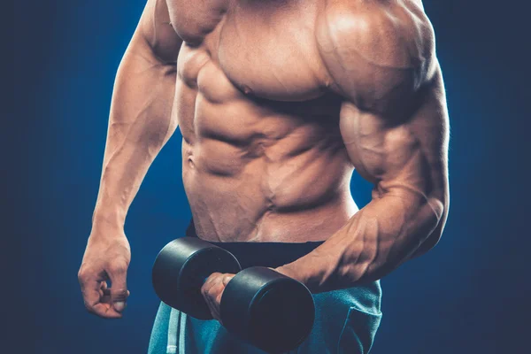 Closeup of a muscular young man lifting dumbbells weights on dar — Stock Photo, Image