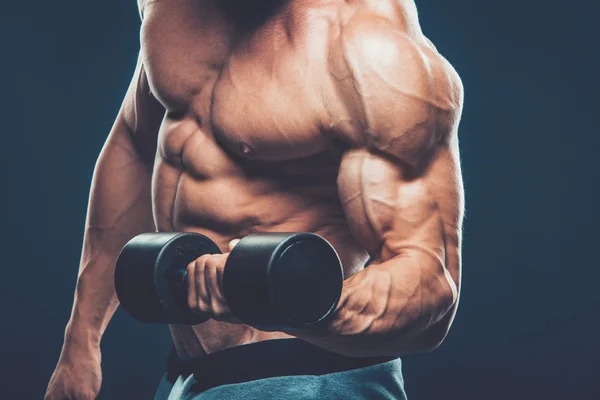 Closeup of a muscular young man lifting dumbbells weights on dar — Stock Photo, Image