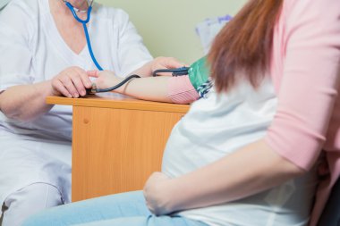 Doktor klinikte hamile bir kadının kan basıncını ölçüyor.