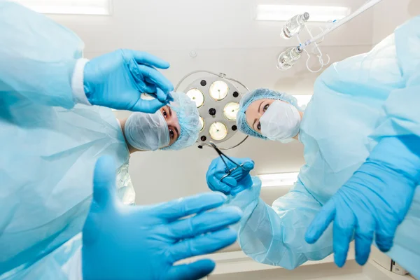 Two surgeons in protective uniform preparing for operation, looking at camera on background of surgical lamp. — Stock Photo, Image