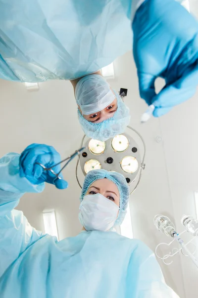 Två kirurger i skyddande uniform förbereder för drift, titta på kameran på bakgrund av kirurgiska lampa. — Stockfoto