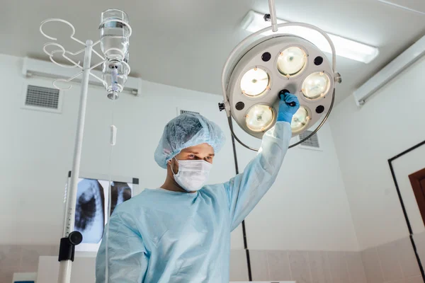 Surgery, medicine and people concept - surgeon in mask adjusting lamp  operating room at hospital — Stock Photo, Image
