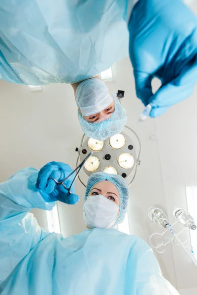 Twee chirurgen in beschermende uniform voorbereiden op operatie, camera kijken op achtergrond van chirurgische lamp. — Stockfoto