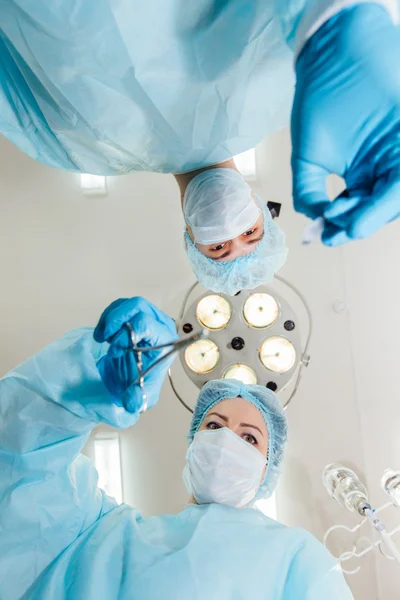 Two surgeons in protective uniform preparing for operation, looking at camera on background of surgical lamp. — Stock Photo, Image