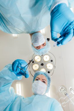 iki cerrah ameliyat lambası arka plan üzerinde kameraya bakarak koruyucu üniformalı işlemi için hazırlama.