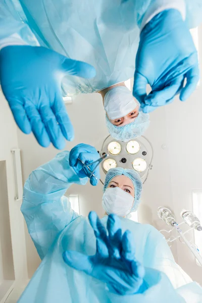 Deux chirurgiens en uniforme de protection se préparent pour l'opération, regardant la caméra sur le fond de la lampe chirurgicale . — Photo