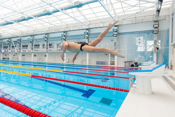Fiatal, izmos úszó ugrás a kezdő blokk egy uszodában — Stock Fotó