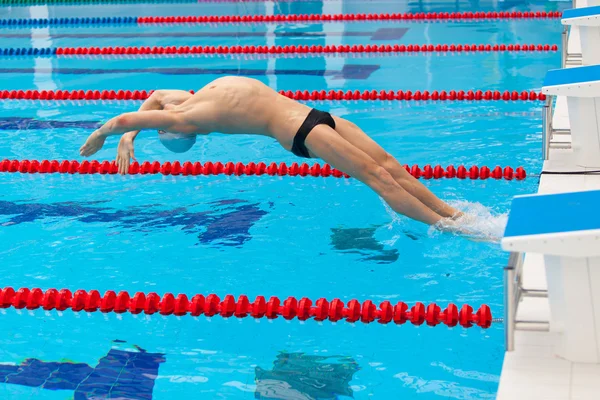 Giovane nuotatore muscolare che salta dal blocco di partenza in una piscina — Foto Stock