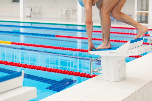 Young muscular swimmer in low position on starting block a swimming pool — Stock Photo, Image