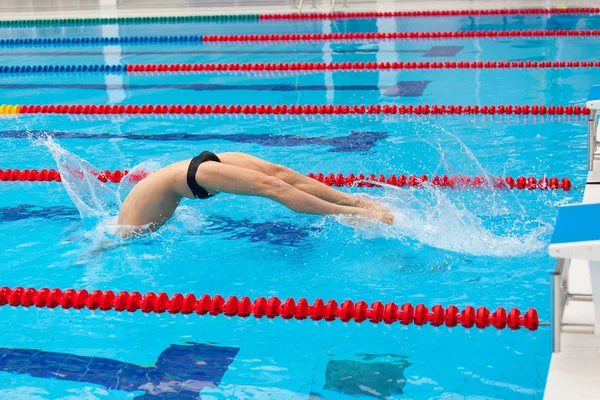 Young muscular swimmer jumping from starting block in a swimming pool — Stock Photo, Image