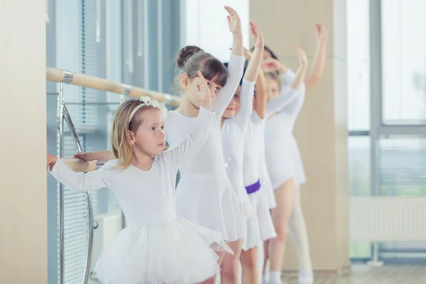 Grupo de siete pequeñas bailarinas de pie en fila y practicando ballet con palo en la pared —  Fotos de Stock