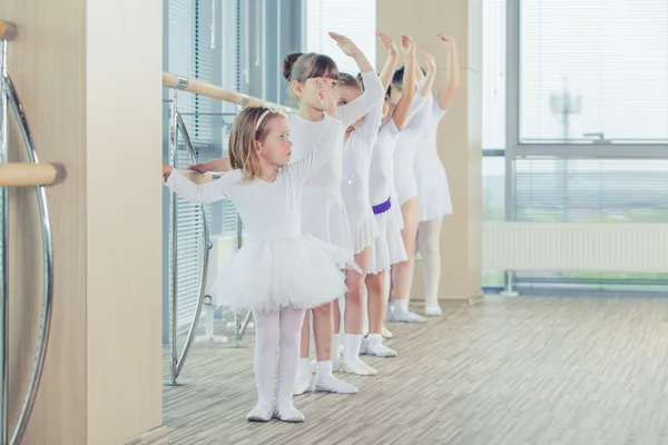 Grupo de siete pequeñas bailarinas de pie en fila y practicando ballet con palo en la pared —  Fotos de Stock