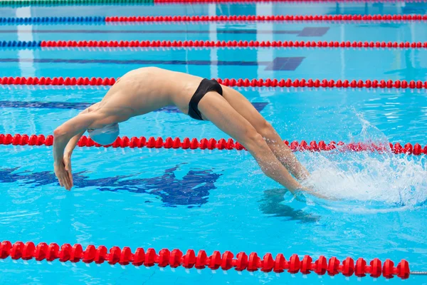 Young muscular swimmer jumping from starting block in a swimming pool — Stock Photo, Image