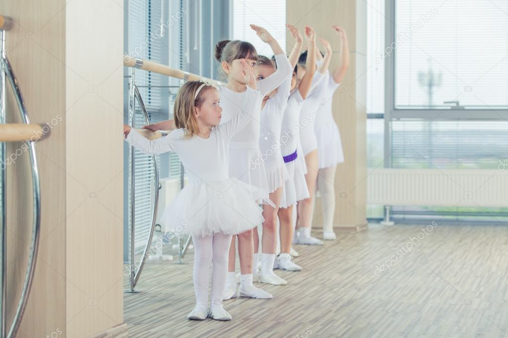 Group of seven little ballerinas standing in row and practicing ballet  using stick on the wall Stock Photo by ©satyrenko 113349480