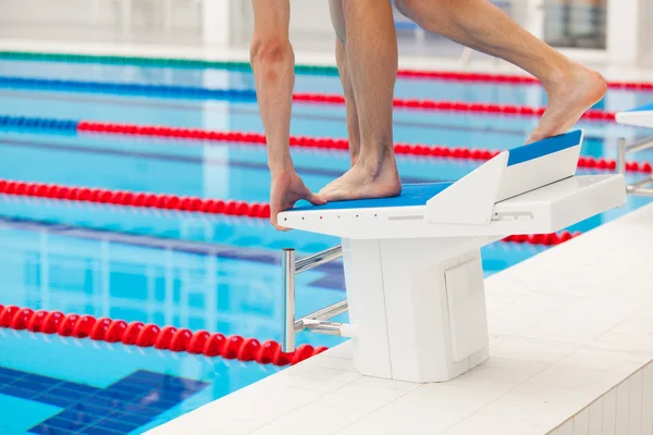 Young muscular swimmer in low position on starting block in a swimming pool — Stock Photo, Image