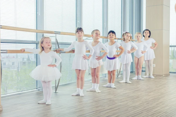 Grupo de siete pequeñas bailarinas de pie en fila y practicando ballet con palo en la pared —  Fotos de Stock