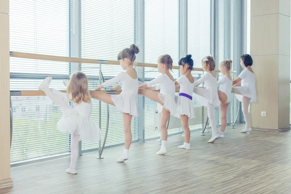 Grupo de sete pequenas bailarinas em pé na fila e praticando balé usando pau na parede — Fotografia de Stock