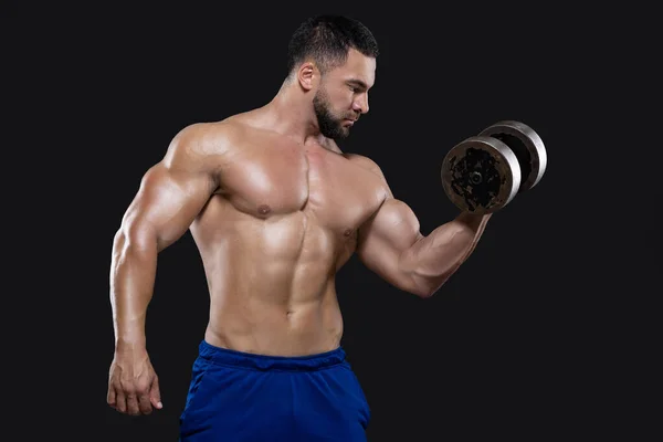 A handsome beefy man is focused on performing the exercise lifting a dumbbell with one hand isolated on black background — Stock Photo, Image