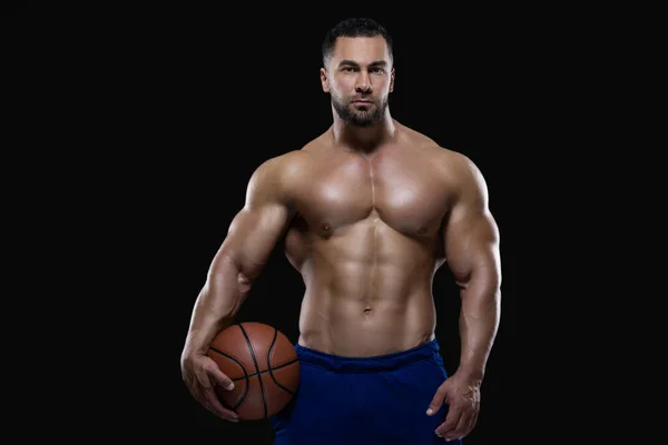 Retrato frontal de un deportista atractivo sosteniendo una pelota de baloncesto con una mano aislada sobre fondo negro — Foto de Stock