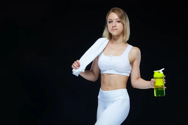 Gyönyörű fiatal sportasszony kezében egy üveg víz és egy sárga súlyzó felett fekete háttér — Stock Fotó