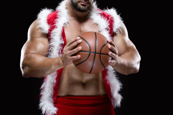 Front view portrait of an attractive muscular Santa Claus holding a basketball with both hands isolated on black background — Stock Photo, Image