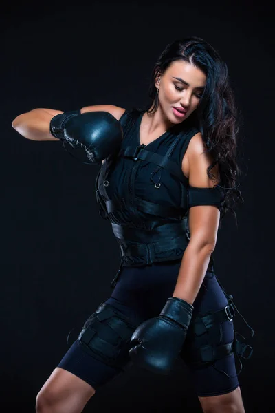一个身穿环球旅行服，戴着拳击手套的年轻女运动员，背景是孤立的黑色。EMS培训。电肌肉刺激机. — 图库照片