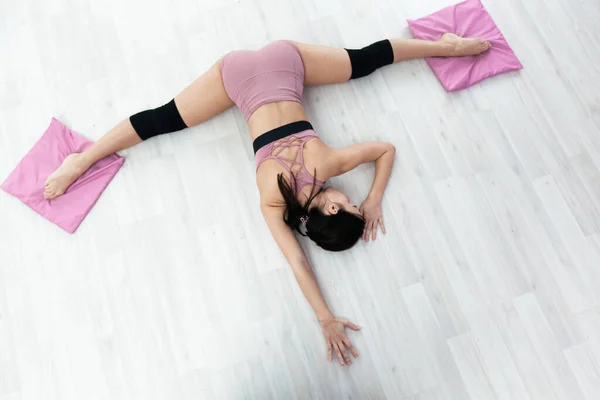Jovem mulher fitness faz exercício de alongamento deitado no chão com os pés em tapetes — Fotografia de Stock