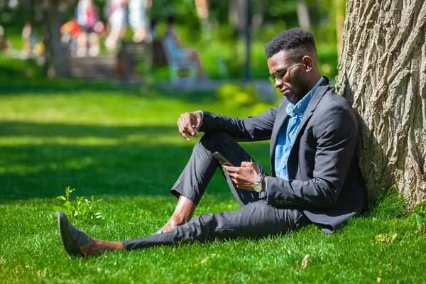 Afro-Amerikan bir adamın parkta bir ağacın yanında cep telefonuyla mesaj atması gibi şık bir iş. — Stok fotoğraf