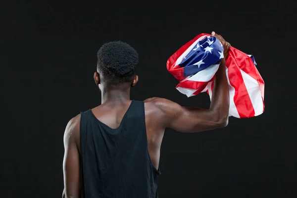 Vue de dos de l'homme tenant le drapeau américain dans une main levée isolée sur fond noir. Concept de patriotisme, amour de la Patrie, symbole national — Photo