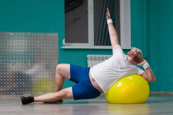 Smiling fat man is doing exercises using fitness ball. Overweight man is happy with the result of his training in group fitness classes — Stock Photo, Image