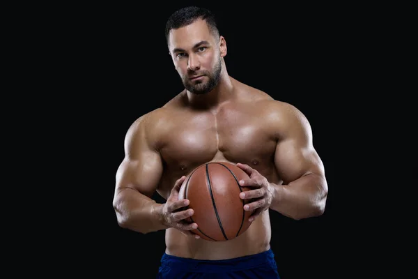 Retrato frontal de un deportista atractivo sosteniendo una pelota de baloncesto con ambas manos aisladas sobre fondo negro — Foto de Stock