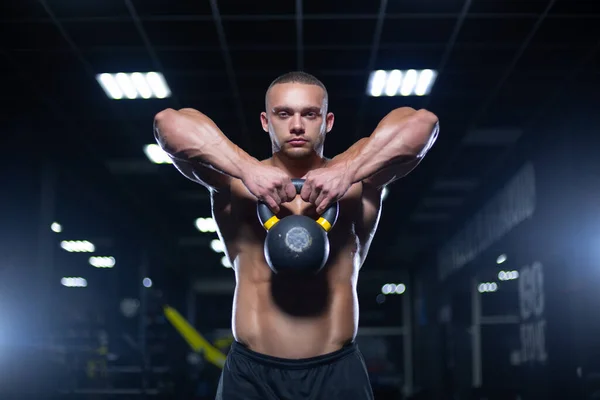 肌肉发达的健美运动员正在他前面提起水壶，在体育馆里锻炼他的手臂肌肉 — 图库照片