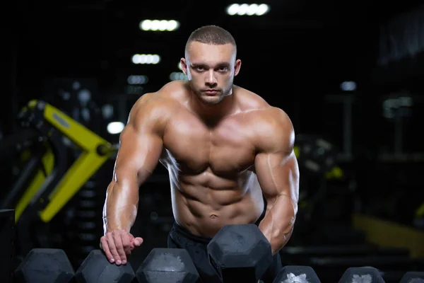 Culturista adulto joven está eligiendo una mancuerna para el levantamiento de pesas de entrenamiento en el gimnasio —  Fotos de Stock