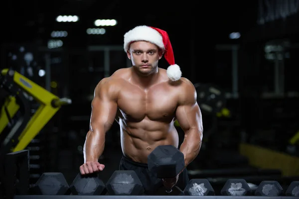 Atleta Joven Optimista En Ropa Deportiva Negra Y Sombrero De Santa  Sonriendo Y Mirando A La Cámara Mientras Hace Ejercicio Con Pesas El Día De  Navidad Contra El Fondo Gris Fotos, retratos