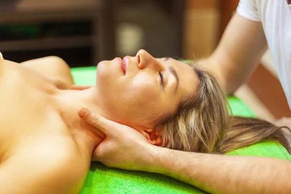 Close up of beautiful young woman lying on her back relaxing with neck massage at beauty spa — Stock Photo, Image